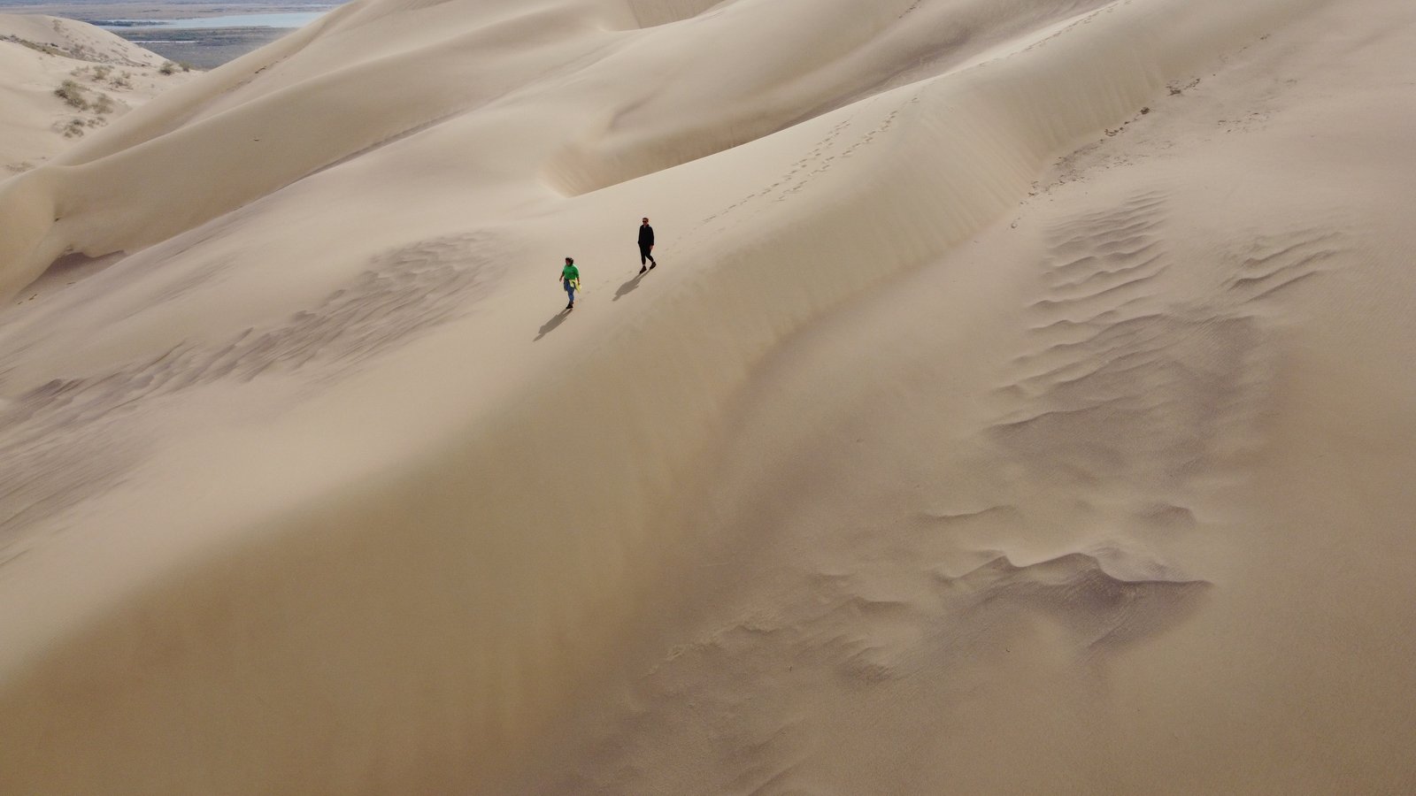 Drone view of two visitors descending the Singing Dune face — Altyn-Emel National Park, Kazakhstan