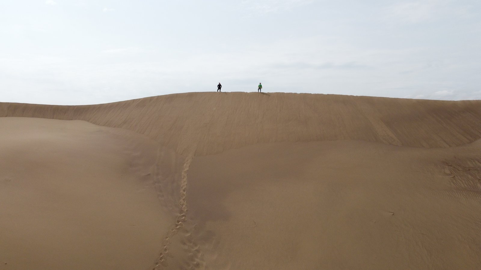 Two visitors on the crest of the Singing Dune — aerial view, Altyn-Emel