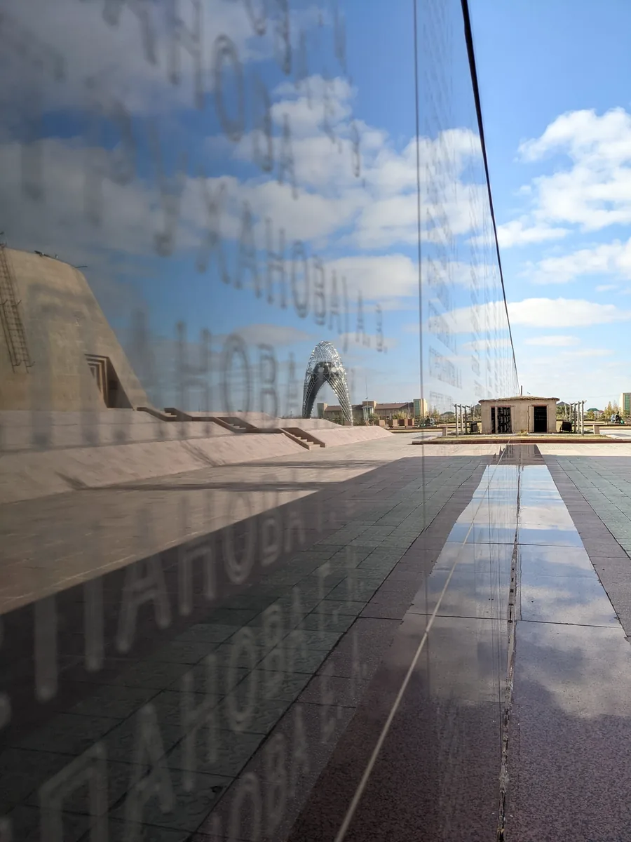 ALZHIR memorial wall with names of victims reflecting sky and Nur-Alem tower, Astana Kazakhstan