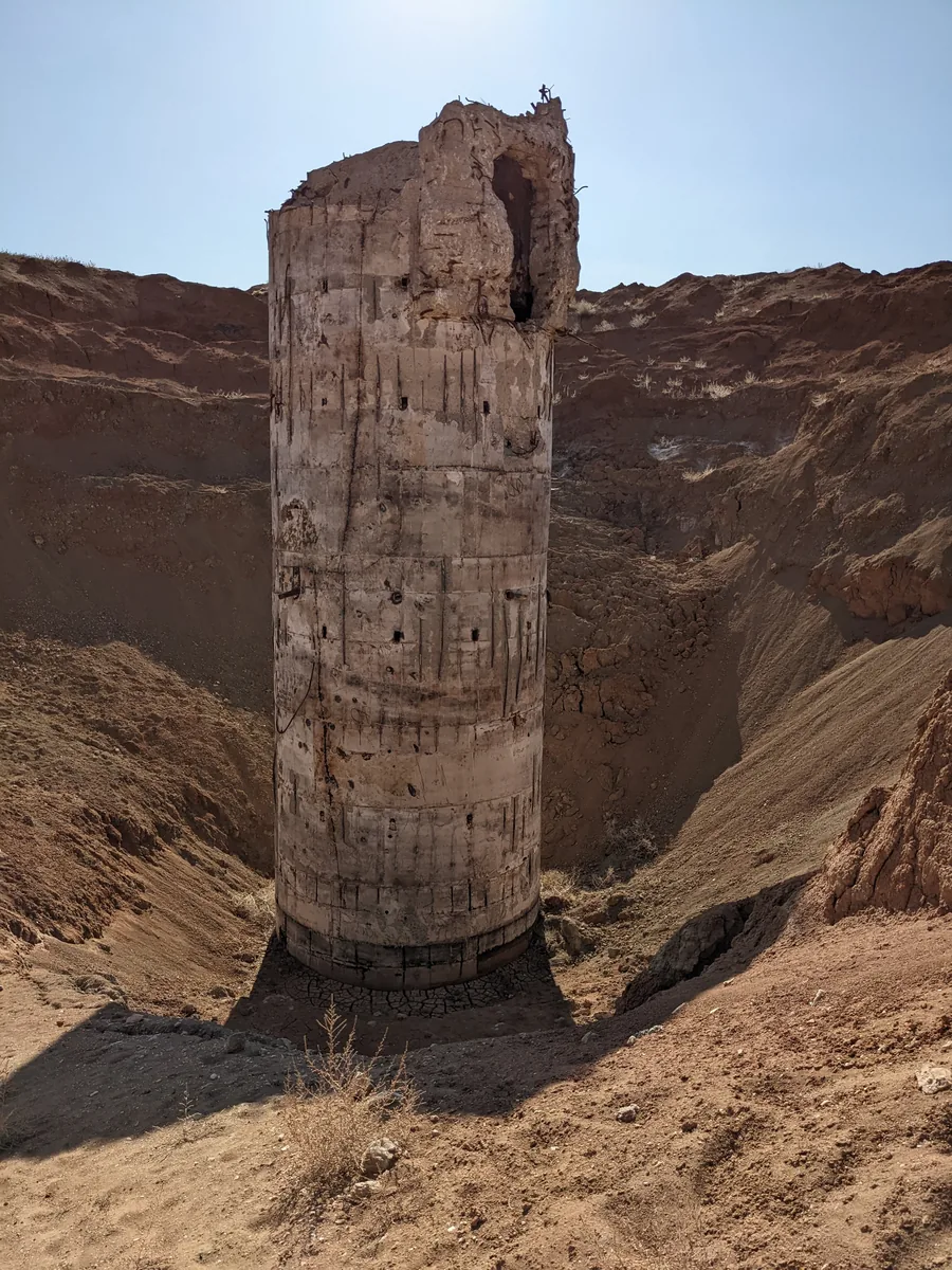 Crumbling concrete cylinder structure rising from red earth canyon, Kazakhstan steppe