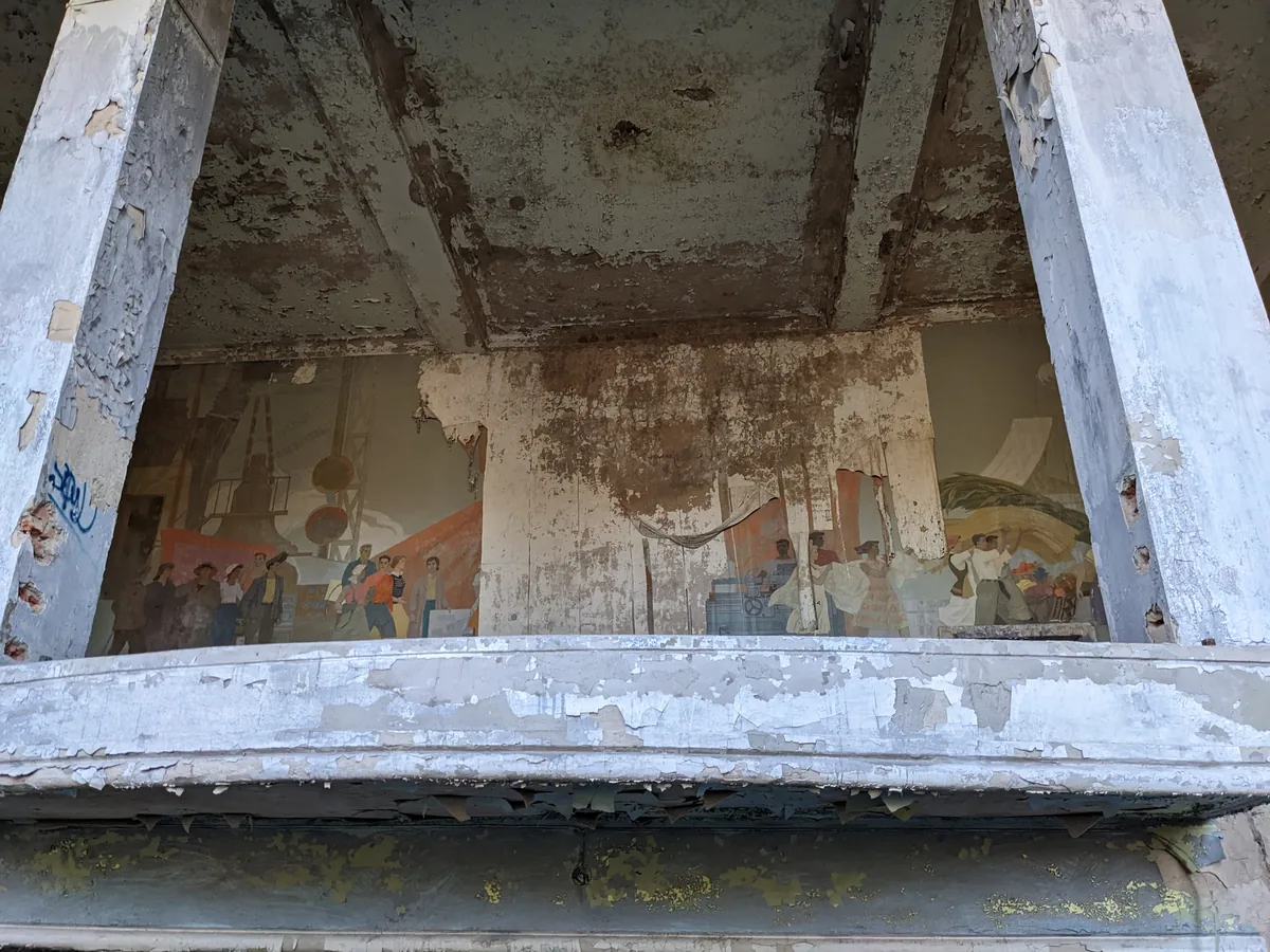 Faded Soviet-era propaganda mural visible through ruined building window frame, Kazakhstan