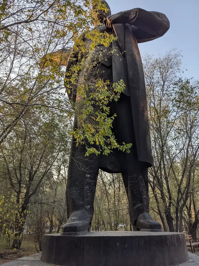 Headless Soviet-era statue overgrown with autumn vines in a Kazakhstan city park