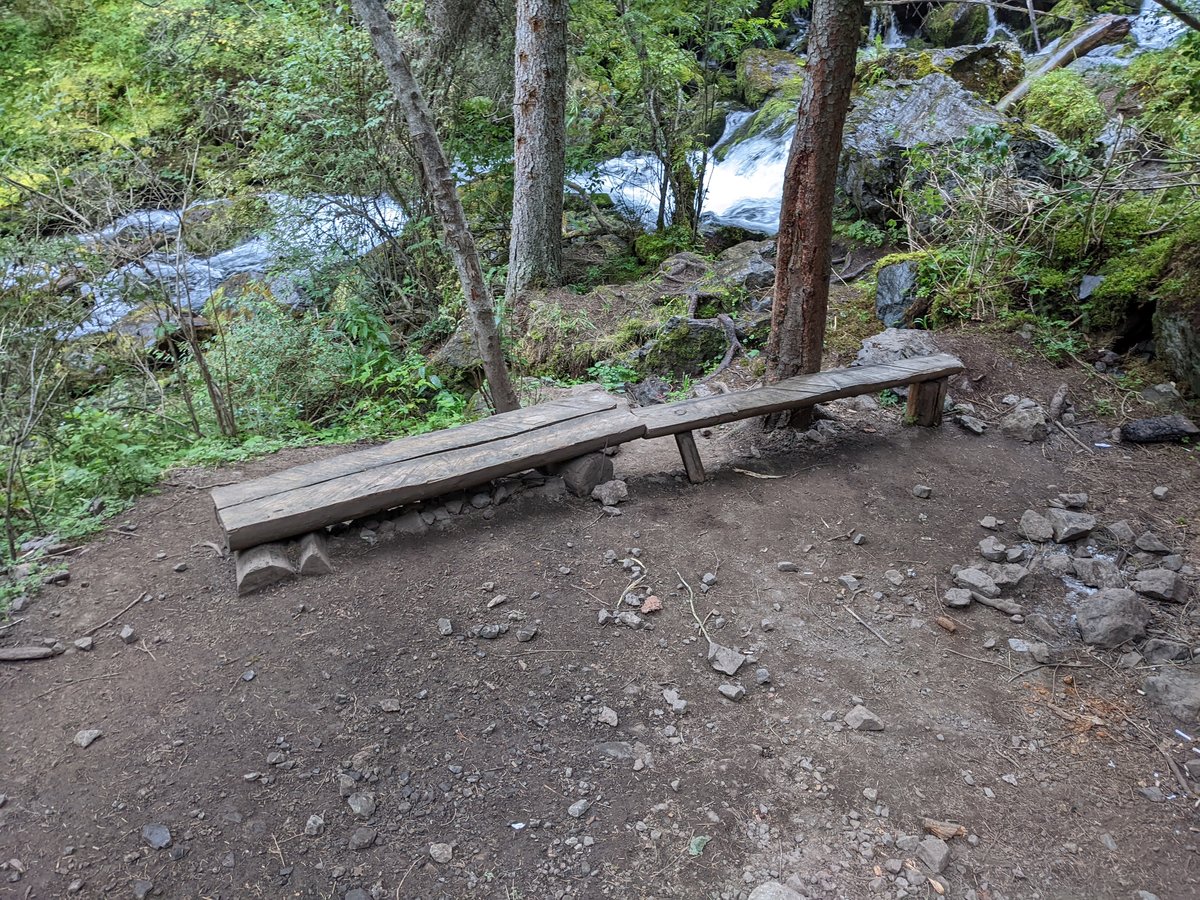 Wooden bench by mountain waterfall on the Kolsai trail — rest stop in the forest